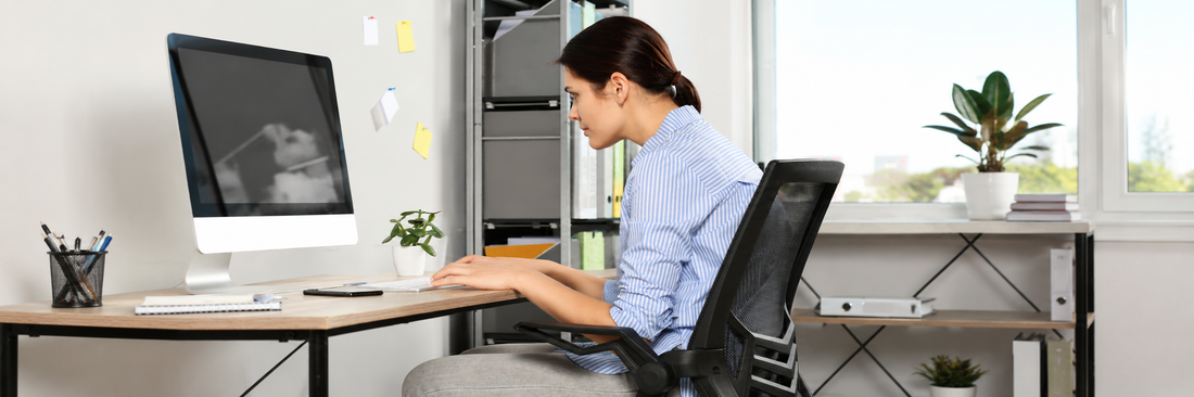 A young woman sitting in a slouching posture while typing on a personal computer in an office